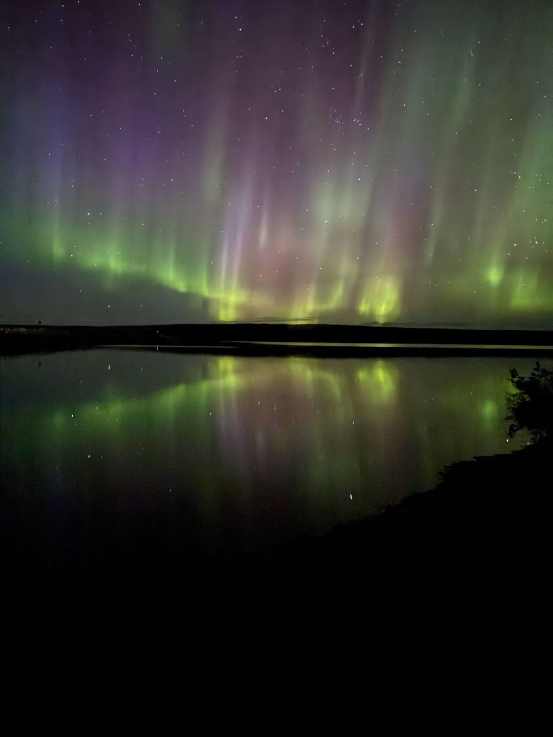 Green and purple Northern Lights reflected in a calm lake at night