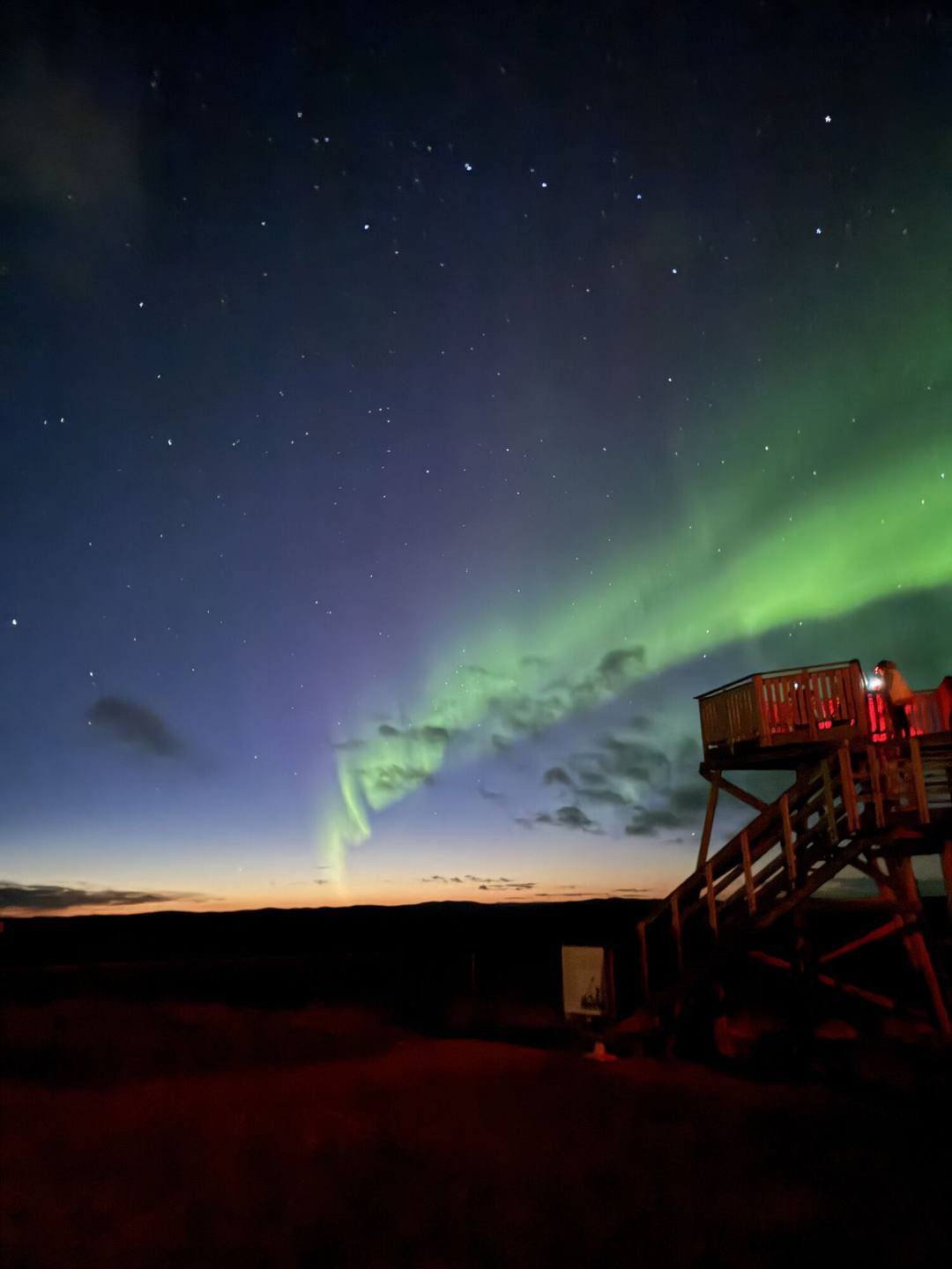 Green aurora over a wooden lookout tower at twilight