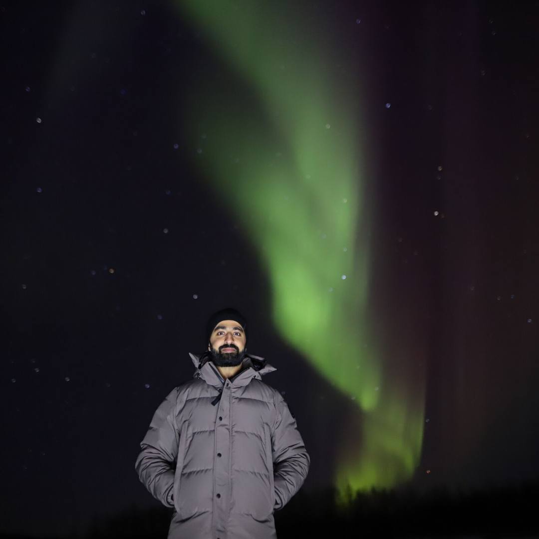 Guest in a grey winter jacket under green Northern Lights
