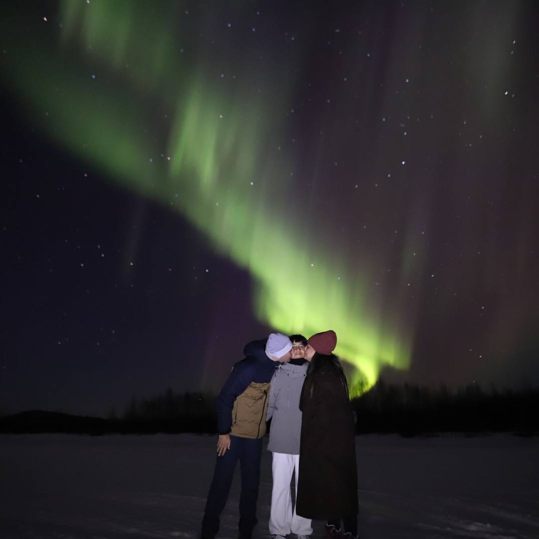 Guests embracing on snow under a green aurora